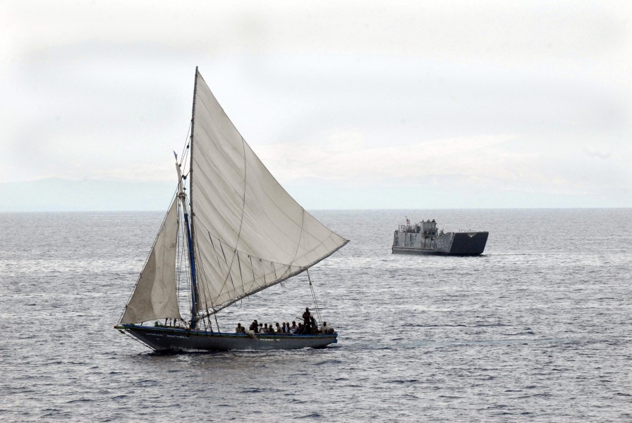 US Navy 100119-N-2000D-023 A Haitian boat sails near a U.S. Navy landing craft unit transporting supplies and equipment in support of Operation Unified Response