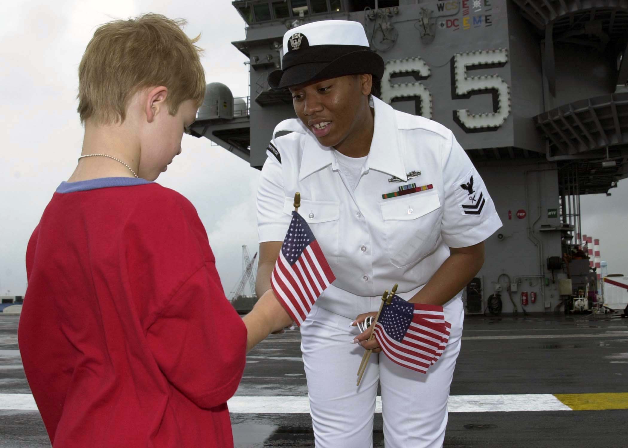 US Navy 040429-N-6268K-012 Intelligence Specialist 2nd Class Tashawbaba McHerrin hands an American flag to a child on the ship's flight deck