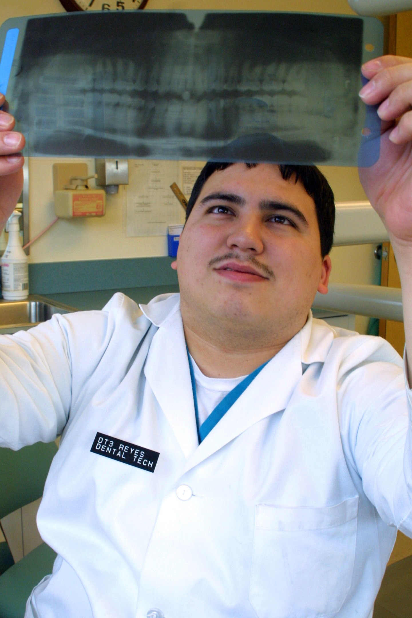 US Navy 050301-N-6620C-022 Dental Technician 3rd Class Jorge Reyes holds an x-ray up to the light as he studies a patient's teeth
