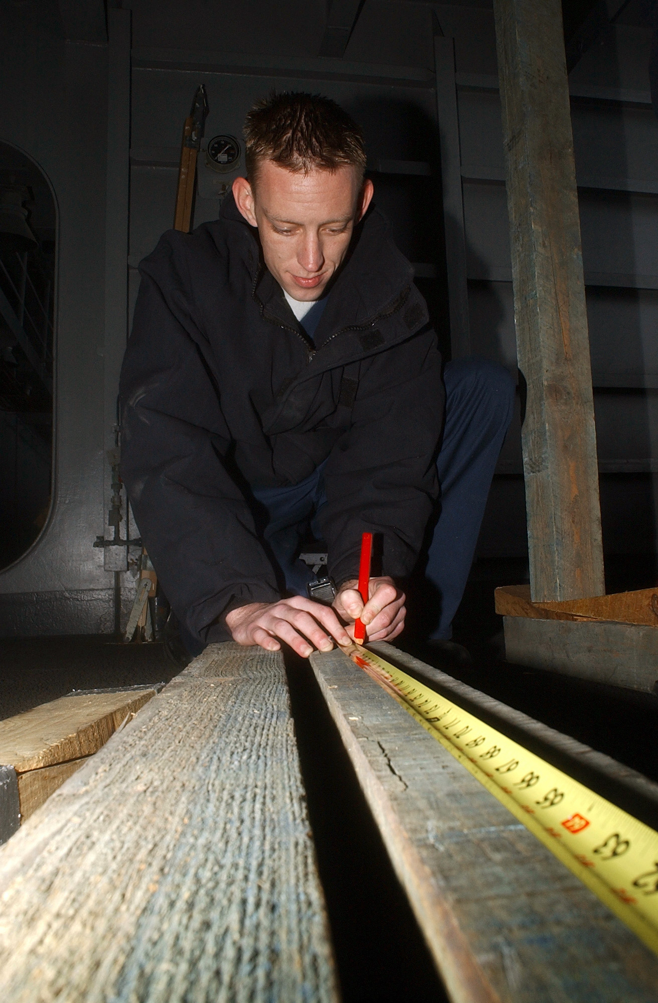 US Navy 050411-N-7405P-038 Damage Controlman 3rd Class Marc Robins measures wood before cutting it