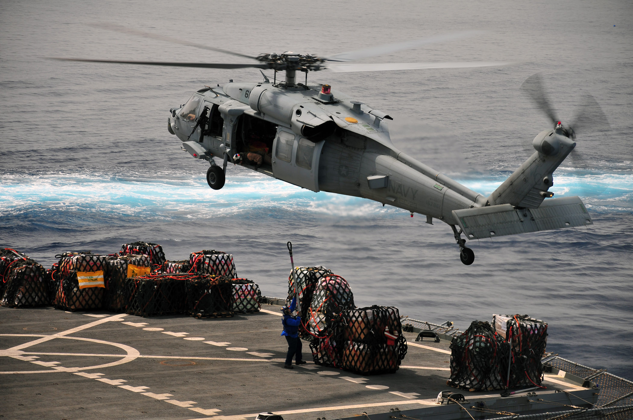 US Navy 110330-N-ZS029-488 A merchant marine prepares to attach a cargo net to an MH-60 Sea Hawk helicopter en route to USS Green Bay (LPD 20)